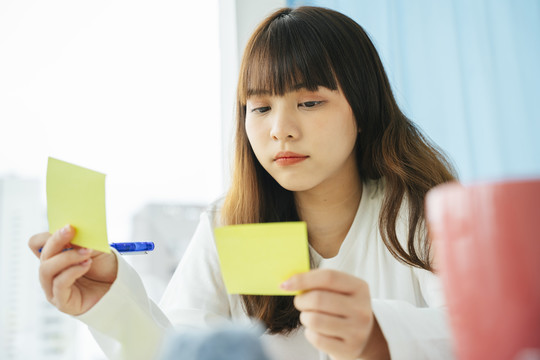 年轻的亚洲黑发女子在便笺纸上写作和计划。