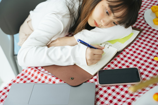 无聊的亚洲年轻黑发女子躺在桌子上，一边在家写书。