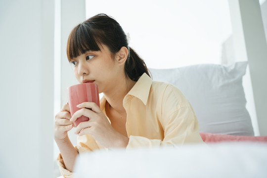 年轻的亚洲黑发女人在卧室里喝咖啡。