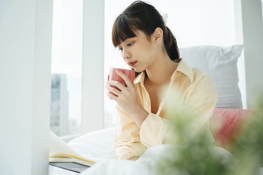 年轻的亚洲黑发女人在卧室里喝咖啡。