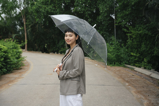 侧视图-穿着正式衬衫手持透明伞的亚洲女商人的时尚肖像。