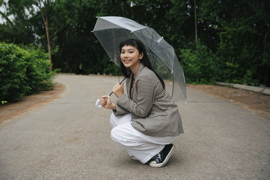 穿着正式衬衫的亚洲女商人手持透明雨伞坐在街上的时尚写真。