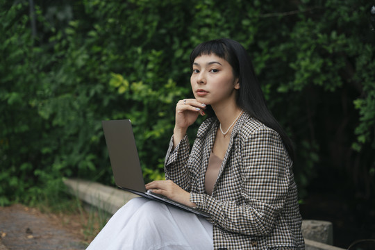 穿着正式衬衫的亚洲女商人在户外使用笔记本电脑。