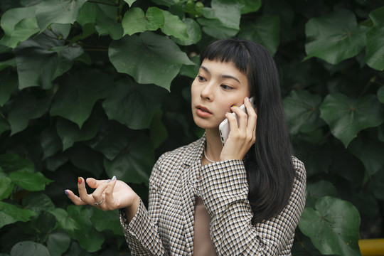 穿着正式衬衫的亚洲女商人在自然背景下使用智能手机。