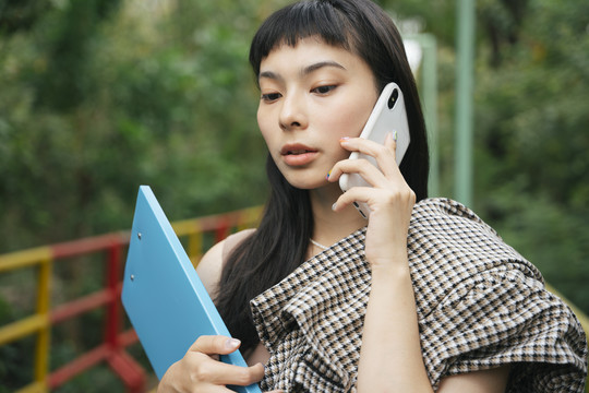 穿着正式衬衫的亚洲女商人拿着文件夹在电话里交谈。