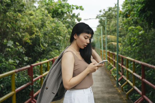 侧视图-穿着正式衬衫的亚洲女商人在户外使用智能手机。