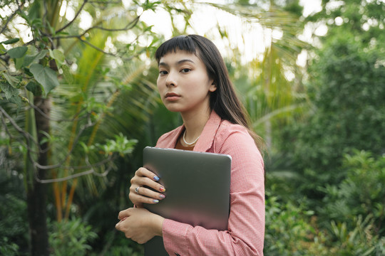 穿着正式衬衫的亚洲女商人，手里拿着笔记本电脑。