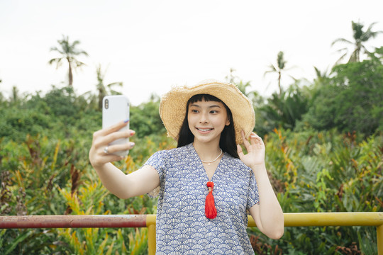亚洲旅行女性戴草帽用智能手机自拍的时尚写真。