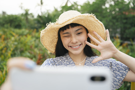 亚洲旅行女性戴草帽用智能手机自拍的时尚写真。