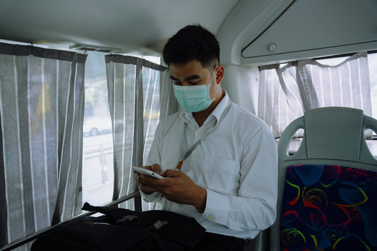 亚洲商人在公共汽车里戴着口罩用手机。