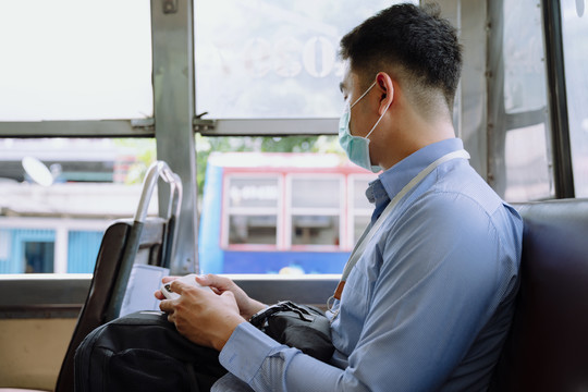 在公共汽车上使用智能手机的亚洲商人。