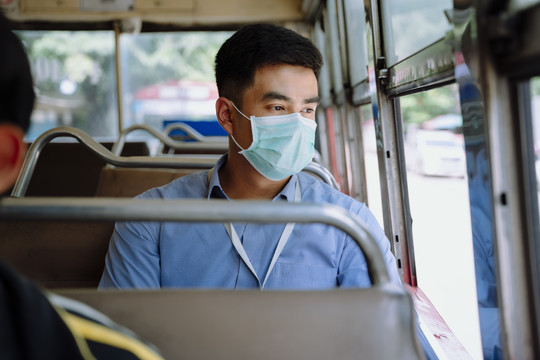 亚洲商人戴着面具在曼谷乘公共汽车旅行。