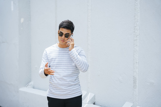 时尚亚洲成年男子戴墨镜打电话的画像。