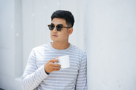 亚洲成年男子戴墨镜捧着一杯咖啡。