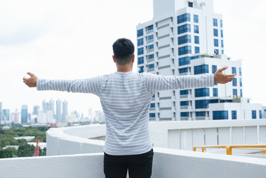 后视图-年轻人站在户外，张开双臂寻求自由和自由。