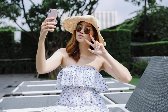 美丽的亚洲女游客戴着帽子和太阳镜用智能手机自拍。