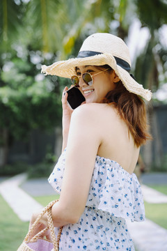 美丽的亚洲女旅行者，戴着墨镜和帽子，在户外使用智能手机。
