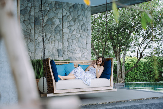 美丽的亚洲女游客在度假酒店泳池边的沙发上休息