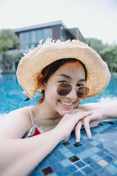 快乐的亚洲女游客戴着墨镜和帽子在游泳池里放松。