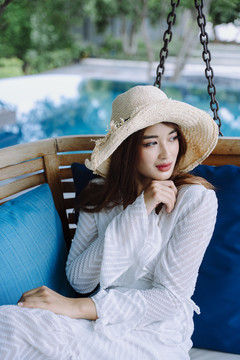美丽的亚洲女游客戴着帽子在酒店休息室靠近游泳池。