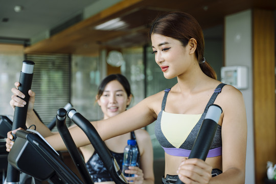 美丽健康的女人在健身房和教练在机器上锻炼。