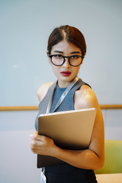 戴眼镜手持笔记本电脑的亚洲女商人的特写照片。