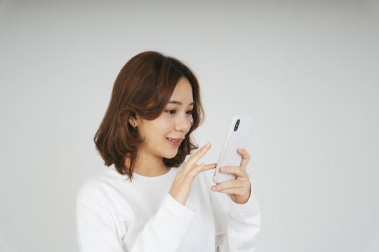 一位年轻的亚洲女性，戴着白色背景的智能手机。