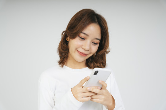 一位年轻的亚洲女性，戴着白色背景的智能手机。