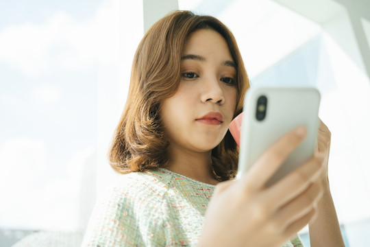 亚洲女人在家里用智能手机聊天喝咖啡。