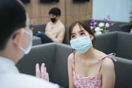 年轻的亚洲女人戴着面具在医院和医生交谈。