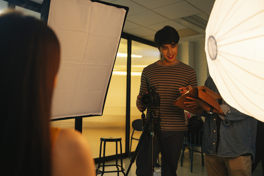 亚洲年轻摄影师，摄影棚里有照相机和暖光。