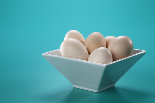白色方形碗，蓝色背景，盛满棕色鸡蛋。摄影棚拍摄。