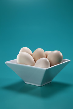 白色方形碗，蓝色背景，盛满棕色鸡蛋。摄影棚拍摄。