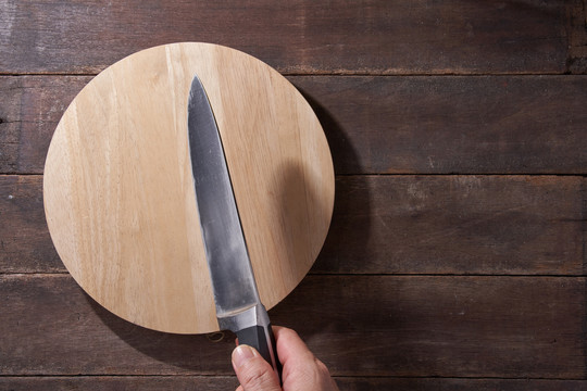 空的圆形木制切板，用于面包、比萨饼或牛排，刀放在厨房的桌子背景上，复制空间。俯视图，平面布置