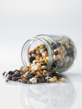 将黑眼豆、绿豆、红豆、黄豆、黑豆和红芸豆混合在白色背景上的泥瓦匠罐中