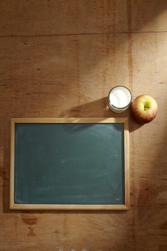 一块空白黑板旁放着苹果和一杯牛奶