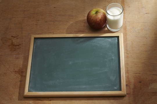 一块空白黑板旁放着苹果和一杯牛奶