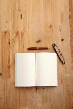 木桌上有带眼镜的空白记事本。上图。