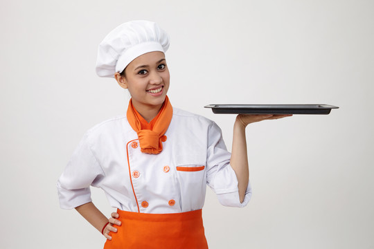 一个穿着厨师制服的印度女人拿着一个空盘子的肖像