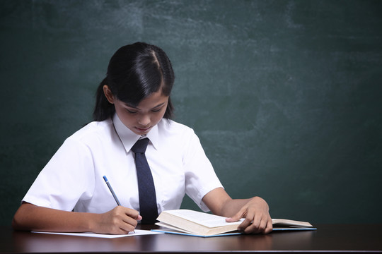 穿制服的女学生在黑板前看书