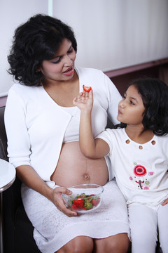 小女孩抱着草莓给怀孕的母亲看