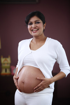 一个年轻漂亮的女人抱着怀孕的肚子，微笑着。