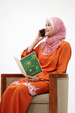 亚洲穆斯林马来妇女，图东手持瑞亚贺卡，用手机交谈