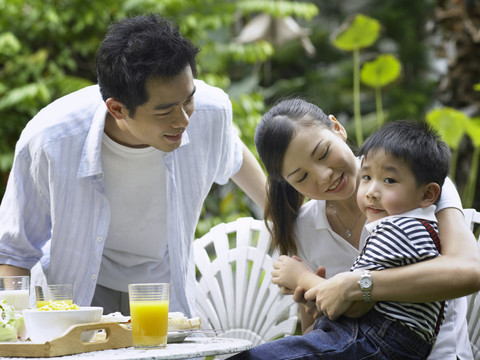 一对年轻夫妇和他们的儿子在花园里吃早餐