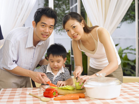 一对夫妇抬头看着摄像机，和儿子在厨房准备食物