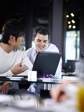 两个男人在咖啡馆里用笔记本电脑，微笑着