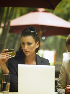 一位女商人坐在外面的咖啡馆里，用笔记本电脑看信用卡