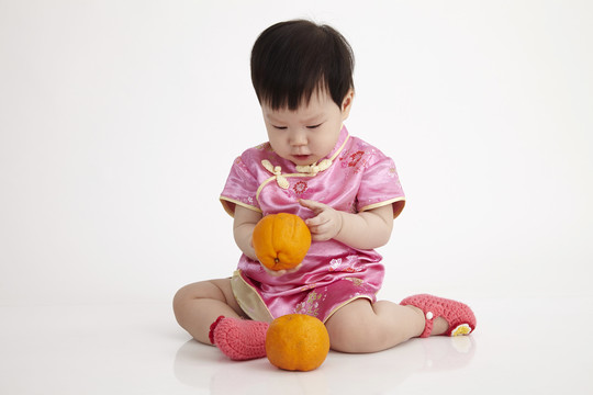 一个中国婴儿穿着雪松，手里拿着桔子