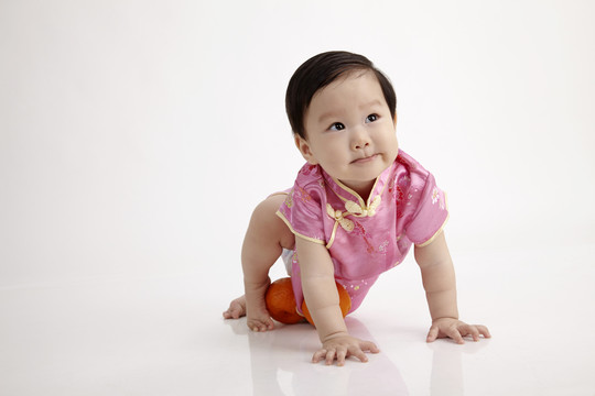 穿着旗袍在白色背景上爬行的中国婴儿
