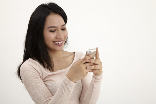 快乐美丽的年轻女子短信和上网与她的智能手机隔离在白色背景